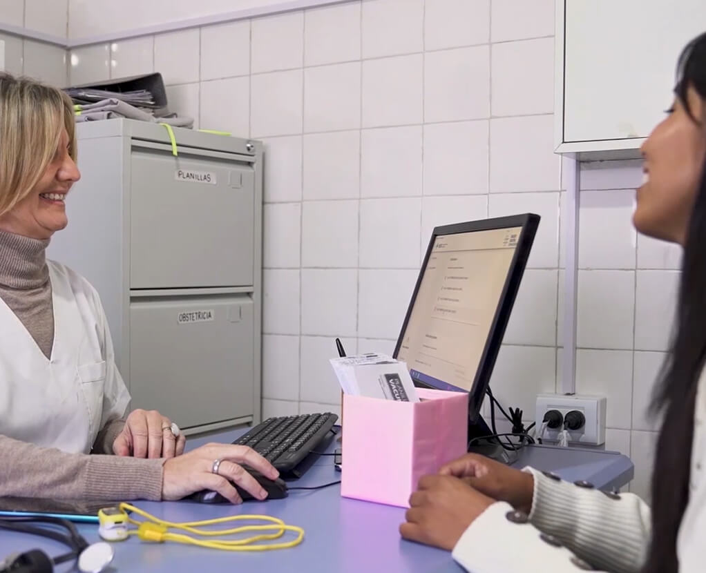 Una profesional de salud sonriente atiende a una paciente frente a una computadora en un consultorio médico de la red atendiendo Chagas.